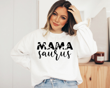 A woman smiling and wearing a white long-sleeved sweatshirt with the text 'MAMA saurus' in black font.